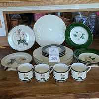 Front view of assorted china plates and mugs arranged in pile and row, showing floral patterns and some with green rim.