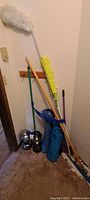 Cleaning tools including mops, dusters, and two blue folding chairs leaning against a wall near some camping lanterns on the floor.