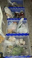 Multiple plastic blue bins filled with assorted Christmas holiday decorations including plastic greenery, artificial flowers, bear figurines, wrapped delicate ornaments, and other various holiday decor items.
