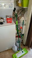 View of the green mop leaning against a white washer or dryer, with cleaning supplies and bags in the background
