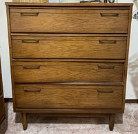 Front view of solid wood dresser showing four drawers with brass-colored handles and tapered wooden legs.