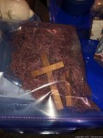Plastic bag containing multiple brown wooden crosses mixed with Easter grass, likely Easter decorations.