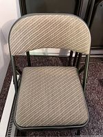 Close-up of beige folding chair with cushioned seat and back covered in beige patterned fabric.