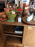 Wide view of various kitchen items on a wooden surface including pottery, salt and pepper shakers on a turntable, terracotta pots, and containers with utensils.