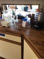KitchenAid food chopper and various kitchen glass and plastic containers, measuring cups, and kitchen accessories on wood counter