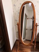 Front view of oval standing mirror with natural wood frame and stand showing the full height and oval glass.