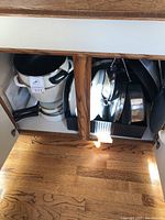 View inside a cabinet showing multiple stainless steel pots and frying pans with some lids, mostly Encore brand.