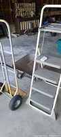 Photo showing the step ladder and the moving dolly placed side by side on the concrete floor.