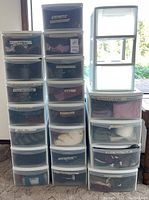 Stacked plastic storage bins with clear drawers labeled for organization of various clothing types such as skirts, knitwear, and jackets