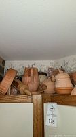 Top shelf view of terracotta kitchenware including casserole dish, pitcher, bowls, and a rolling pin.