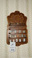 Wooden rack with 19 thimbles arranged in rows against floral wallpaper, with identification tag 408 visible.