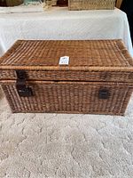 Front view of rectangular wicker chest with lid, resting on carpeted floor
