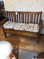 Front view of the wooden mission-style bench with three floral cushions on the seat, showing the vertical slat back and armrests.
