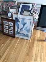 Framed floral artwork, architectural sketches, smaller framed art, and small clock grouped on floor and couch.