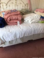 Bedding items including quilts, blankets, and pillows arranged on a bed with a brass headboard.