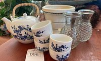 Photo showing blue and white porcelain teapot, five matching teacups, two clear textured glass vases, and white ceramic planter with black rim trim