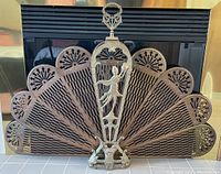 Full view of decorative brass fireplace screen showing fan-shaped perforated panels and central figural handle.