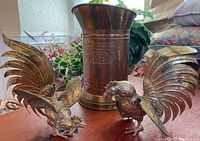 Photo showing two brass rooster fighting figurines and the large brass pitcher in the background