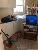 Wood rolling cart in laundry room with mop, buckets, men's clothing, and blue recycling bin on top