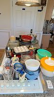 View of assorted kitchen cookware including bowls, measuring cups, and baking pans arranged on stove and counter.