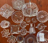 Top view of assorted cut glass serving ware pieces arranged on a wooden surface, includes plates, trays, bowls, creamers, and small dishes with intricate cut patterns.
