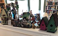 Multiple Two Country Lane and Brandywine decorative items including birdhouses, clown statues, and miniature buildings on display by a windowsill