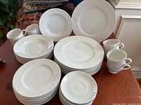Full view of dinnerware set items stacked and arranged on table showing plates, bowls, and cups.