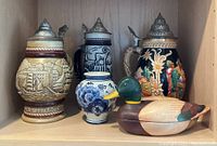 Group photo of three German-style beer steins, a Delft vase, and a wooden mallard decoy on a shelf
