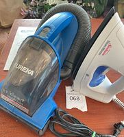 Photo showing both Eureka handheld vacuum and Sunbeam iron on a wooden surface