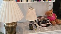Photo of two lamps, two puzzle boxes titled 'Upwords' and a teddy bear wearing a pink shirt on a shelf.