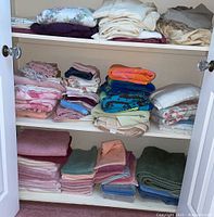 Shelving unit with stacks of assorted folded linens and towels, various colors including pastels and floral prints