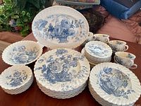 Full set displayed on table with stacked plates, bowls, and cups showing the blue floral basket pattern on white china.