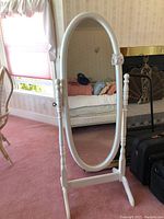 Front view of the full-length oval mirror with white wooden frame, standing upright in a bedroom setting, showing its size relative to surroundings.