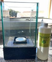 Photo showing glass enclosure fire pit with black base and circular metal fuel container inside.