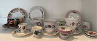 Wide shot of assorted floral fine china and porcelain teacups with matching saucers displayed in a row.