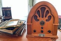 Front and angled view of Thomas Collectors Edition Radio with wood finish and ornate speaker grill, accompanied by assorted picture frames stacked next to it.