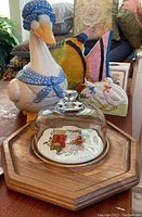 Photo of ceramic goose cookie jar wearing blue polka dot bonnet and scarf, wooden tray with glass dome covering serving dish with fruit motif