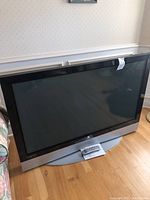 Front view of Vizio TV resting on its stand, with remote and instruction booklet visible beneath it.