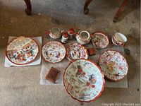 Wide view of the entire set showing multiple plates, teapot, cups, salt shakers, and coasters arranged on floor.