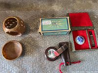 Photo of carved stone candle holder, shallow dish base, box, red velvet case with signature stamps and ink pad, leather pouch, and small boxed switch.