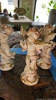 Photo showing three Capodimonte cherub figurines playing instruments arranged on a wooden surface