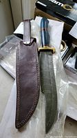 Collector's blade and brown leather sheath laid side by side on plastic wrapping.