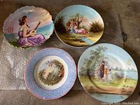 Four decorative plates arranged on bubble wrap showing detailed painted images.