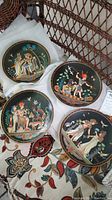Photo of four black porcelain plates with painted Egyptian scenes, arranged on fabric and packing material