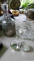 Full view of glass decanter with hammered pewter holder, glass bowl with Christmas tree, and two etched glass eggs on table.
