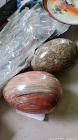 Photo showing two polished marble eggs, one in red and grey stripes and the other in grey tone with intricate patterns.