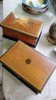 Two wooden music boxes on table, one with a shield emblem on top and the other with a floral inlay.