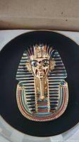 Close-up photo of the collector plate featuring the front view of Tutankhamun's gold, blue, and multicolor death mask on a black porcelain background.
