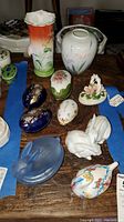 Various porcelain and glass decorative items including vases, trinket boxes, bunny figurines on wooden surface.