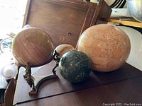 View of all four spheres together on a surface, showing size and color variations, including the brass stand for one sphere.